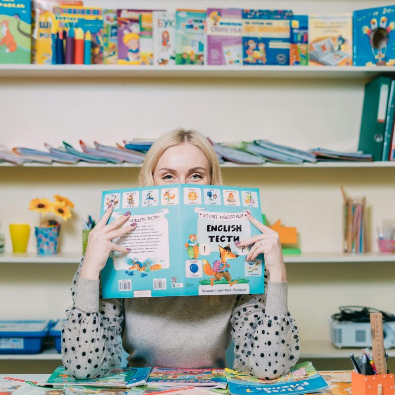 pexels-photo-9310201-9310201-1 Woman reading an English book in a colorful classroom setting.
